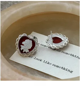 Detailed macro view of vintage red heart cameo earrings with rose relief and silver lace edges