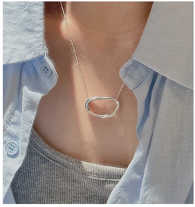 Close-up of minimalist silver oval pendant necklace worn on neck with linen shirt
