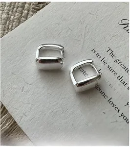 Détail des boucles d'oreilles carrées polies en argent S925 sur un support papier vintage
