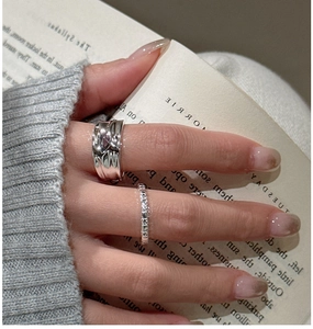 Close-up of a wide textured silver ring and a slim patterned band worn on fingers