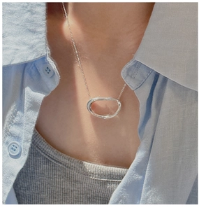 Close-up of S925 sterling silver oval pendant necklace worn on neck with linen shirt