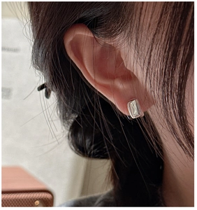 Gros plan de créoles rectangulaires en argent poli au design minimaliste portées à l'oreille