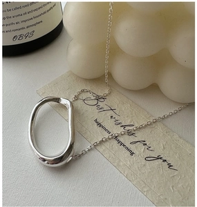 Detail of minimalist S925 silver oval pendant necklace on a textured card