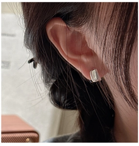 Gros plan d'une boucle d'oreille rectangulaire argentée minimaliste portée sur l'oreille