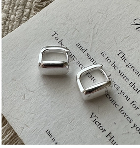 Gros plan de boucles d'oreilles créoles carrées en argent sur un support en papier