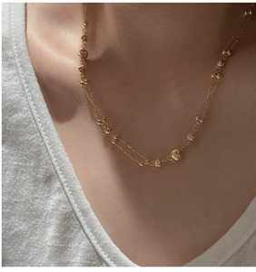 Detail view of a layered gold S925 silver beaded necklace worn on a model's collarbone