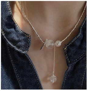 Detail of silver Y-shaped necklace with translucent beads and hollow metal ball on denim