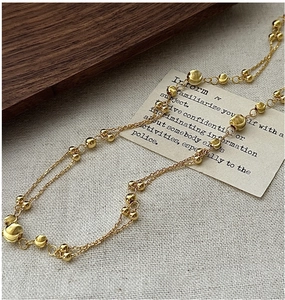 Detail of double-layer golden bead necklace on vintage card and gray texture background