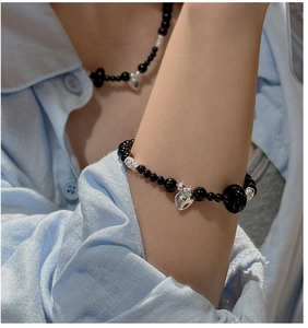 Detail shot of a black bead bracelet with a silver heart pendant on a model's wrist