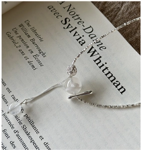 Close-up of S925 silver necklace with translucent bead and metallic bar on vintage book