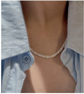Close-up of a silver braided chain necklace worn on the collarbone with a blue shirt