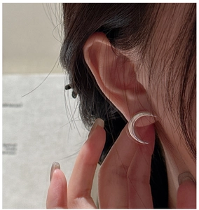 Macro close-up of polished silver crescent moon earrings on a model earlobe