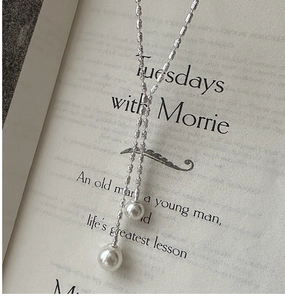 Close-up of S925 silver fringe necklace with white pearls on a book page backdrop