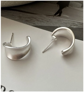 Close-up of minimalist matte 925 sterling silver C-shape hoop earrings on a magazine background