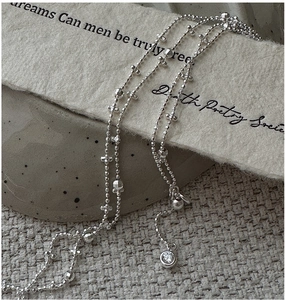 Macro shot of silver beaded necklace with tiny cross charm and clear round crystal pendant