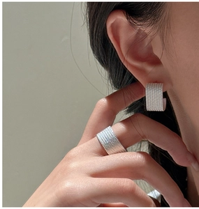 Macro shot of S925 sterling silver earrings and ring with woven texture on model