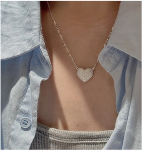 Detail of 925 sterling silver heart necklace with retro texture on blue shirt
