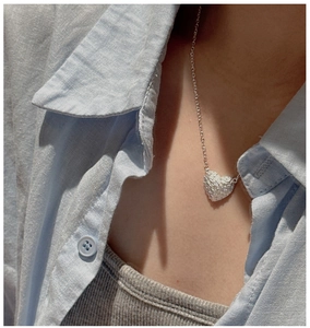 Detailed close-up of a silver heart pendant with unique textured finish on a neck chain