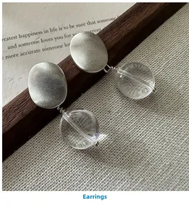 Detailed shot of matte silver oval earrings with clear spherical pendants on wood
