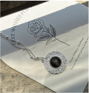 Macro shot of silver necklace with textured round pendant and obsidian gemstone