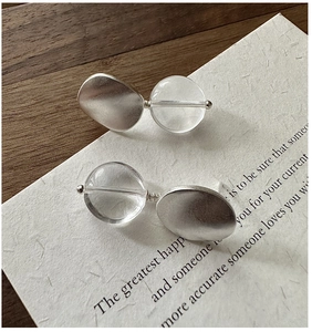 Macro detail of matte silver earrings with clear resin beads on a vintage paper background