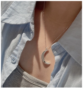 Silver crescent moon pendant necklace worn on a light blue linen shirt in natural light