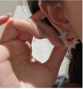 Detailed close-up of C-shaped silver earrings with sunburst textured resin design