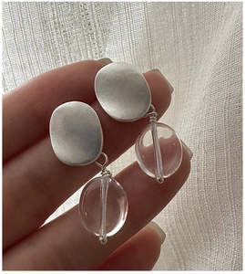 Detail of matte silver oval earrings with clear crystal bead drop held by hand