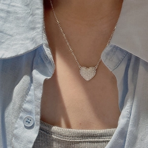 925 silver heart necklace with hammered texture worn on a light blue linen shirt model