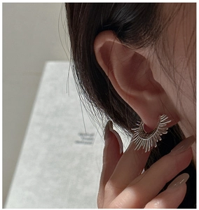 Macro view of silver sunburst fan earrings showing textured metallic lines on ear