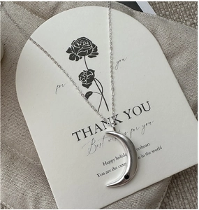 Macro view of a silver crescent moon pendant with black detail on a gift card