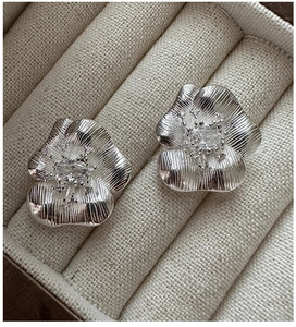 Detail of silver S925 flower earrings with brushed texture and sparkling zircons