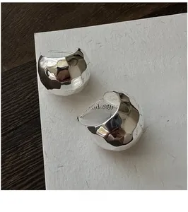 Macro detail of silver earrings with irregular hammered texture and metallic sheen