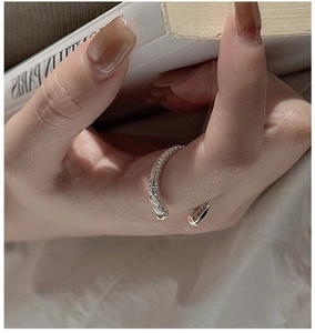 Détail d'une bague argentée à texture torsadée tenue sur un fond de livre minimaliste