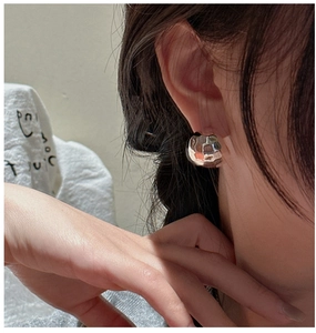 Macro detail of silver geometric hoop earrings with a textured hammered finish on ear