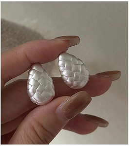 Macro detail of silver teardrop earrings with intricate woven texture and matte finish