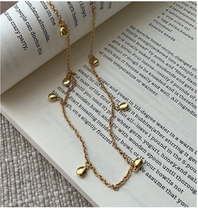 Détail du collier à gouttes d'argent S925 doré posé sur une page de livre vintage
