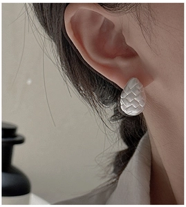 Macro side view of silver woven texture stud earrings on a model with matte finish