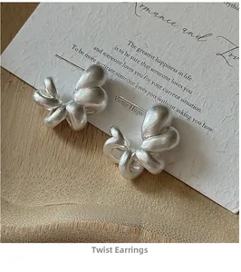 Detailed close-up of matte silver twisted hoop earrings on a minimalist white card