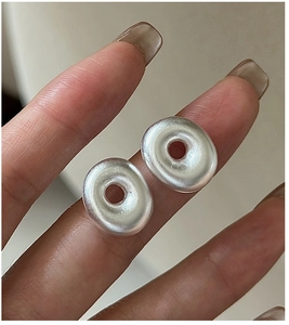 Macro shot of silver matte hollow oval stud earrings held by hand for detailed texture