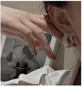 Macro shot of silver C-shaped earrings with fine ribbed texture on a model's ear