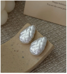 Macro shot of silver teardrop earrings with woven texture on a stone base