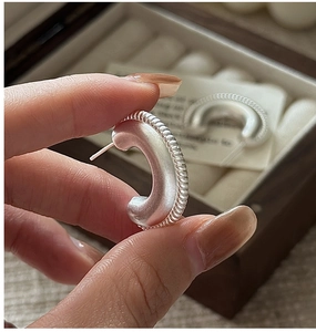 Macro detail of silver C-shaped matte hoop earrings with a textured twisted rope edge
