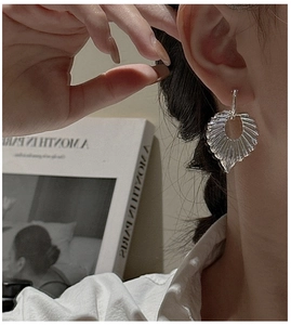 Close-up of a silver shell-shaped earring with vertical stripes on a female model