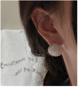 Detail of silver spherical stud earrings with textured mesh pattern worn on ear lobe