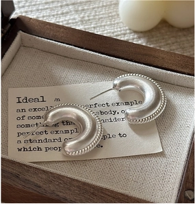 Detail of matte S925 silver hoop earrings with relief twisted rope texture on linen