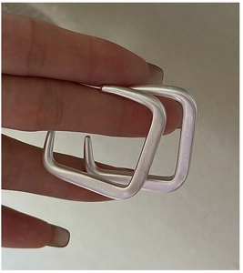 Gros plan de boucles d'oreilles carrées en argent mat avec texture brossée minimaliste