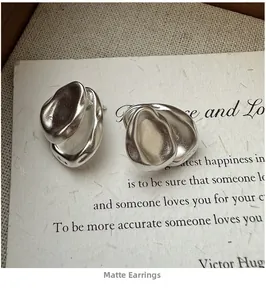 Close-up of matte silver irregular water drop earrings on textured paper with poem