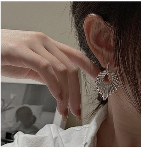Detailed view of silver hollow fan-shaped earrings with pleated leaf texture on a model