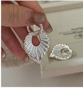 Macro shot of silver hollow leaf earrings with textured sunburst metal details